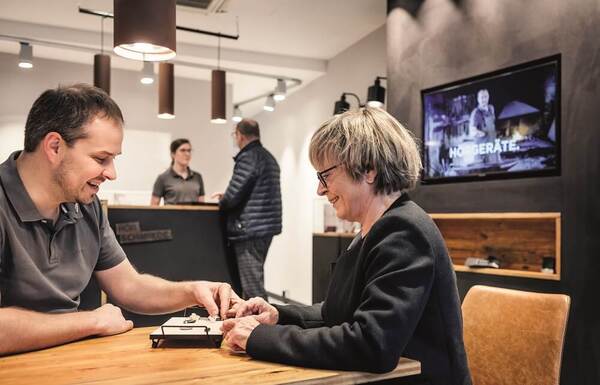 Ein Hörakustiker berät eine ältere Frau freundlich zu modernen Hörgeräten im Fachgeschäft.